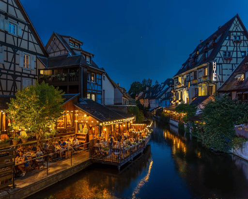 An evening restaurant by a river with charming buildings on the river banks.