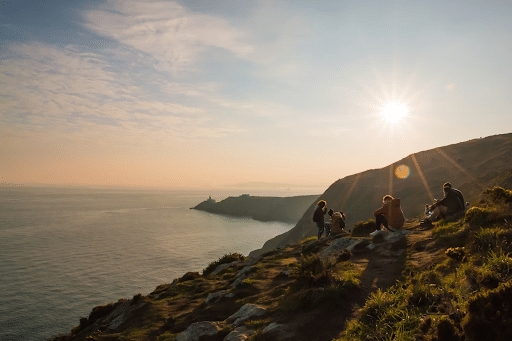 Group of people sitting on a grassy hill overlooking the ocean just outside Dublin