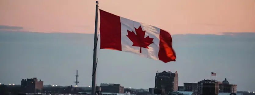Canadian flag flying over a cityscape with the sun setting